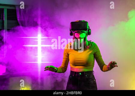 Wireless technologies. Young woman using virtual reality glasses in the dark room with neon lighting. Stock Photo