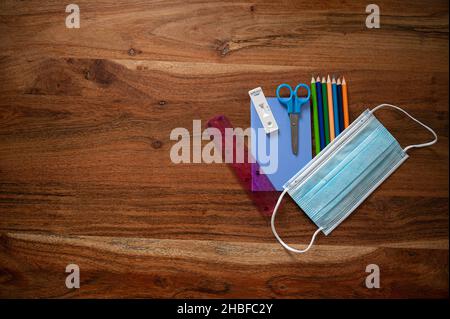 Back to school in coronavirus pandemic conceptual image with protective medical mask over color pencils, scissors, ruler, notepad, and covid19 testing Stock Photo