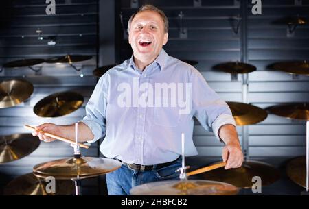Musician male is choosing drum set and playing on it in music shop. Stock Photo