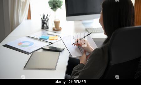 Business woman taking a notes on her personal notebook, listing a work list on her planner book, checking her meeting schedule on a schedule book. Stock Photo