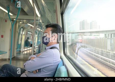 Asian man commuter with face mask on inside a moving subway train. Masked transit concept. Stock Photo