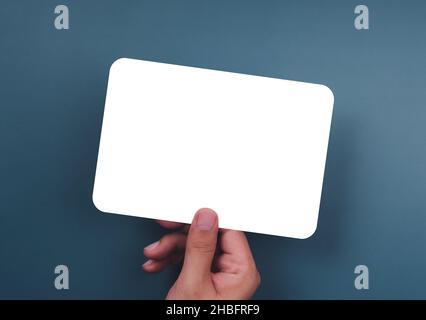 Mockup paper holding with the right hand. Hand holds the white blank mock-up white paper with a rounded corner and a horizontal style on a blue backgr Stock Photo