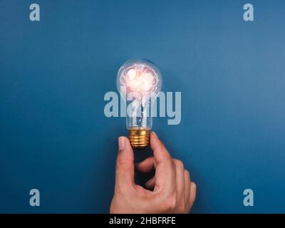Creative, idea, innovation, knowledge, and inspiration concept. The human brain icon is glowing inside the digital light bulb in man's hand on the blu Stock Photo