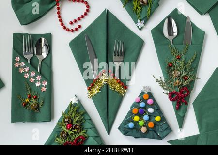 Christmas green color,paper napkins folded in various shapes on white surface with cutlery set and christmas decoration.Top view Stock Photo