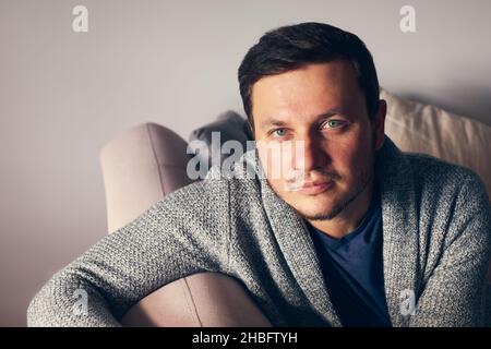 A portrait of man in a cardigan on a pink couch looks into the camera. Front view portrait.  Stock Photo