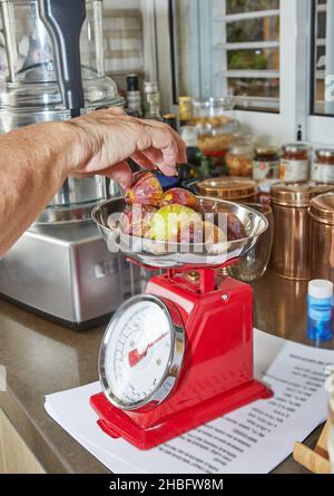 Woman weighs figs on scale in the kitchen to make pie using recipe from the Internet Stock Photo