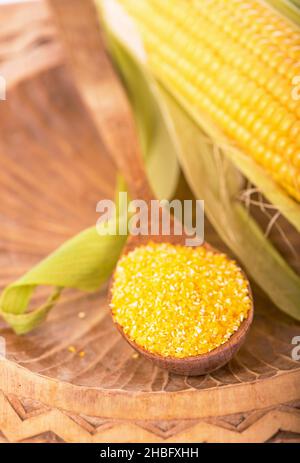 Flour corn in a spoon, cereal in sackcloth and on the table, the cob on the background dark wooden boards Stock Photo