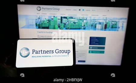 Person holding cellphone with logo of Swiss investment company Partners Group Holding AG on screen in front of webpage. Focus on phone display. Stock Photo