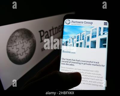 Person holding cellphone with webpage of Swiss investment company Partners Group Holding AG on screen with logo. Focus on center of phone display. Stock Photo