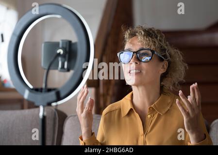 Young modern lady record live podcast with ring light and mobile phone to share on line on tutorial web page. Smart working freelance business caucasi Stock Photo