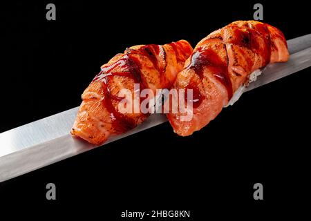 Nigirizushi with fried salmon and unagi sauce on thin blade of Japanese knife isolated on black Stock Photo
