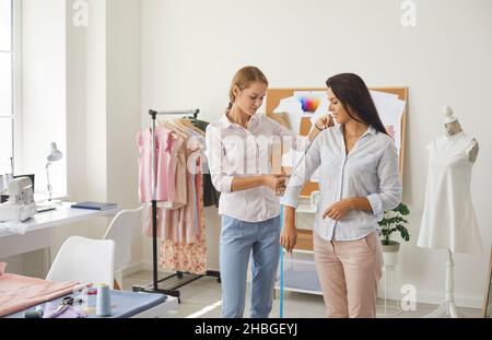 Female fashion designer measures length of client's sleeve for tailored clothes in studio. Stock Photo