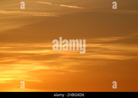 View of the sky at sunset with clouds turning yellow and orange in the evening light for an abstract colorful pattern as a background. Stock Photo
