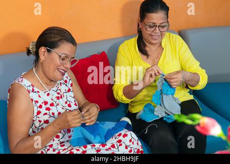 Two Latin women knitting a scarf together at home Stock Photo