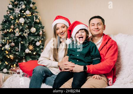 Portrait of happy smiling family with kid son. Laughing mother in Santa hat, father, child boy in sweater having fun on Christmas holidays at home Stock Photo