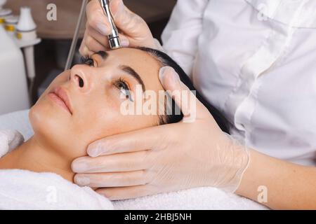 Cosmetologist hands making the procedure Microdermabrasion of the facial skin of a client at the spa salon. Facial skin treatment. Rejuvenation Stock Photo