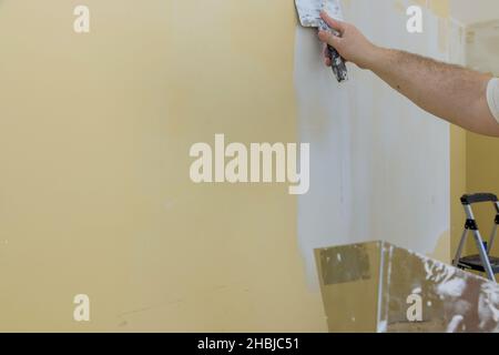 Man plastering the walls with finishing putty in the room with putty spatula Stock Photo