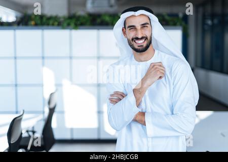 handsome man with dish dasha working in his business office of Dubai. Portraits of a successful businessman in traditional emirates white dress. Conce Stock Photo