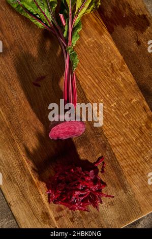 Top view of fresh juicy raw burgundy beetle with tops, half shredded on a grater on a wooden kitchen board. Flat lay. Food background Stock Photo