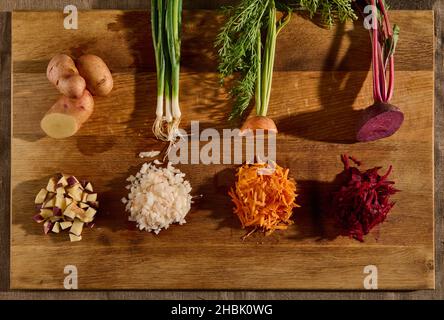 Overhead view of seasonal fresh raw vegetables on a wooden board, cut in half and the other half shredded on a grater. Beets, carrots, green onions wi Stock Photo