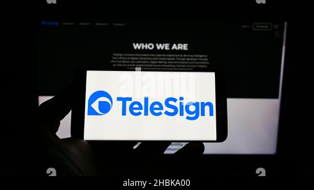 Person holding cellphone with logo of American communications company TeleSign Corporation on screen in front of webpage. Focus on phone display. Stock Photo