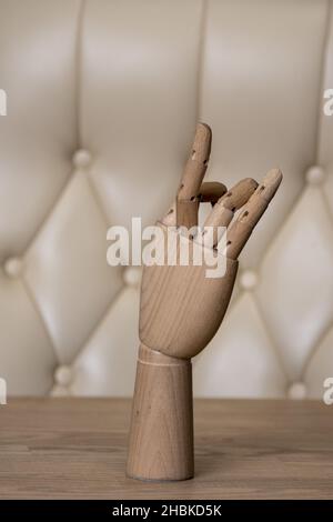 A wooden model of a human hand on a table against the background of a leather chair. Stock Photo