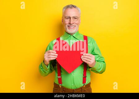 Photo portrait old man smiling in spectacles showing red heart isolated vivid yellow color background Stock Photo