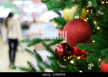 Christmas tree with red toy balls in a shopping mall on festive lights and walking people background. New Year decorations, winter holidays Stock Photo