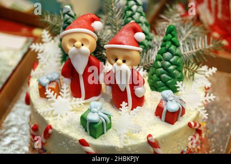 Creamy cake with Santa Claus figures and sweet Christmas decorations in store window. Confectionery, dessert for New year celebration Stock Photo