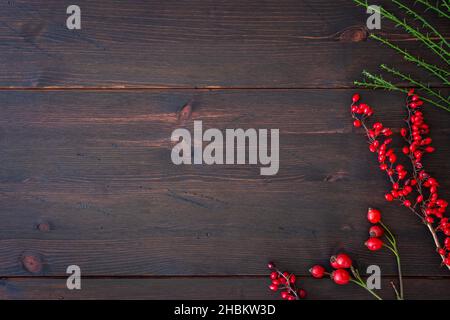 Winter season and Christmas background. Branches of dog rose with rose hip, red barberry on rustic dark brown wooden table. Flat lay design template. Stock Photo