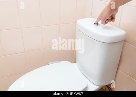 Man hand push toilet flushing button in the bathroom Stock Photo