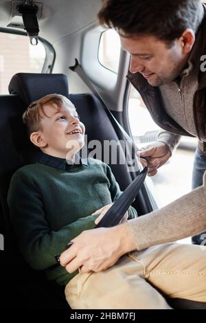 Vertical portrait of man buckling son in back seat of family car Stock Photo