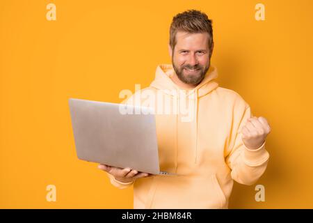 Image of excited young man isolated over orange wall background using laptop computer while making winner gesture. Stock Photo