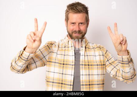 Young smiling man wearing plaid shirt showing peace symbol isolated over white background. Stock Photo