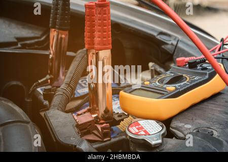 Mechanicl man uses electric multimeter voltmeter to check the voltage level maintenance car battery Stock Photo