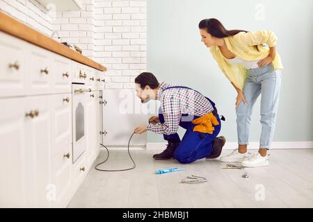 Plumber uses a drain cable to clean a clogged pipe in a young woman's kitchen sink Stock Photo