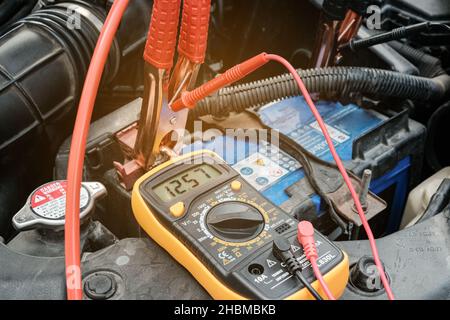 Mechanicl man uses electric multimeter voltmeter to check the voltage level maintenance car battery Stock Photo
