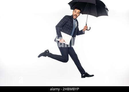 excited businessman in suit jumping with laptop and umbrella on white Stock Photo