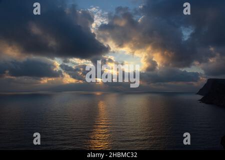 A thundercloud in the orange-yellow light of sunset. Dramatic stormy sky. Huge cumulus clouds over the ocean. A harbinger of bad weather, climate chan Stock Photo