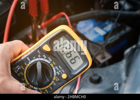 Mechanicl man uses electric multimeter voltmeter to check the voltage level maintenance car battery Stock Photo