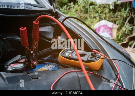 Mechanicl man uses electric multimeter voltmeter to check the voltage level maintenance car battery Stock Photo