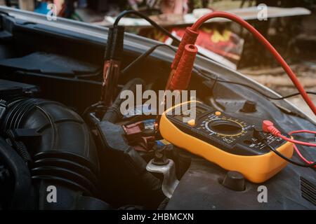 Mechanicl man uses electric multimeter voltmeter to check the voltage level maintenance car battery Stock Photo