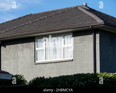 View of detached house with white window frame on gray brick wall and concrete tiles Stock Photo
