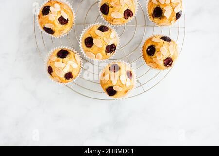 Top view of homemade cherry muffins with almond slivers on silver metal cooling rack over white marble background with lots of copy space. Stock Photo