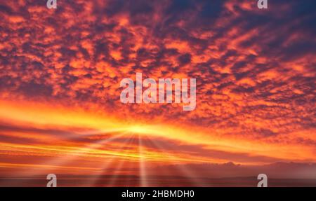 Spectacular sunrise sky in strong, bright yellow, orange and red colors with sun and sunrays. Sky replacement. Stock Photo