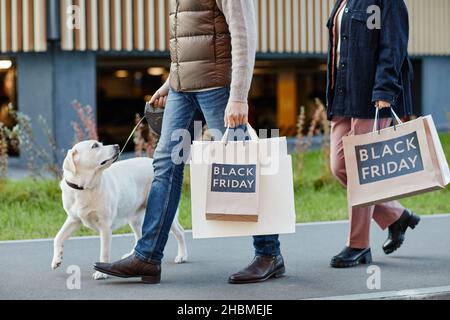 Cropped side view shot of adult couple holding shopping bags with Black Friday while walking outdoors, copy space Stock Photo
