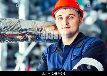 Portrait of young Caucasian engineer worker in helmet in premises of factory workshop. Industrial background. Stock Photo