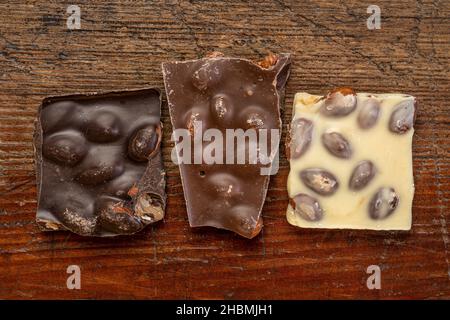 broken pieces of dark, milk and white chocolate with almonds on a rustic wooden table Stock Photo