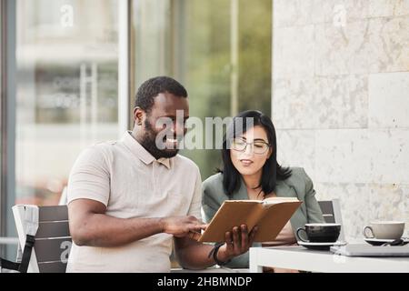 Portrait of smiling African-American man talking to young woman at cafe table outdoors during business meeting Stock Photo