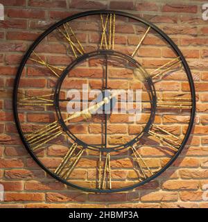 A large circular metal clock on an interior red brick wall with blurred moving hands Stock Photo